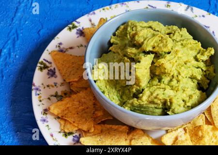 Guacamole in una ciotola blu circondata da nachos su un piatto decorato con fiori. Foto Stock