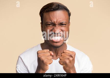 African American Guy Clenching pugni guardando la telecamera, sfondo giallo Foto Stock