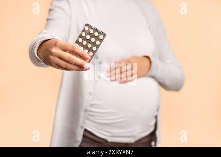 Irriconoscibile la donna incinta che mostra le pillole che posano su sfondo bianco, tagliato Foto Stock