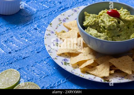 Un bellissimo tavolo blu con guacamole in una ciotola circondata da nachos. Foto Stock