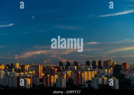 Uno splendido tramonto su una grande città, alti edifici residenziali e grattacieli illuminati dal sole che tramonta contro il cielo blu. Vista da abo Foto Stock