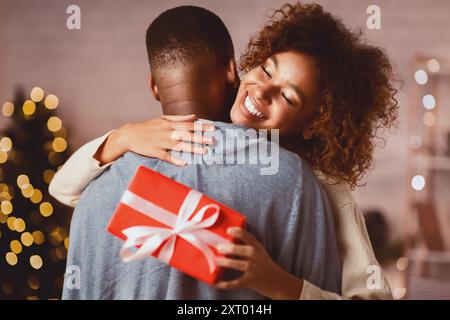 Grati afro donna con un regalo di Natale abbracciando il marito a casa Foto Stock