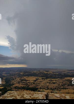 Tempesta sulle colline ondulate: Uno scontro tra le forze della natura. I cieli scuri si stagliano sul paesaggio illuminato dal sole: Un cambiamento climatico drammatico. Contrasto Foto Stock