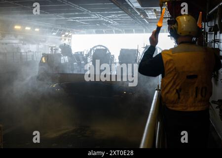 Boatswain's Mate 1st Class Bobby Lynn, nativo di Kansas City, Missouri, segnala a un mezzo da sbarco, cuscino d'aria, assegnato all'Assault Craft Unit (ACU) 5, in quanto esce dal ponte pozzo della nave da carico anfibia classe San Antonio USS Somerset (LPD 25) mentre è in corso nell'Oceano Pacifico, 10 agosto 2024. Somerset è attualmente in corso di operazioni di routine nella 3rd Fleet degli Stati Uniti con elementi della 15th Marine Expeditionary Unit. (Foto della Marina degli Stati Uniti di Evan Diaz, specialista della comunicazione di massa di seconda classe) Foto Stock