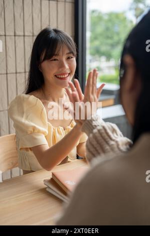 Una bella e allegra donna asiatica sta dando un cinque alto al suo amico mentre è seduta insieme in una stanza. lavoro di squadra, amicizia, collega, brainstorming Foto Stock