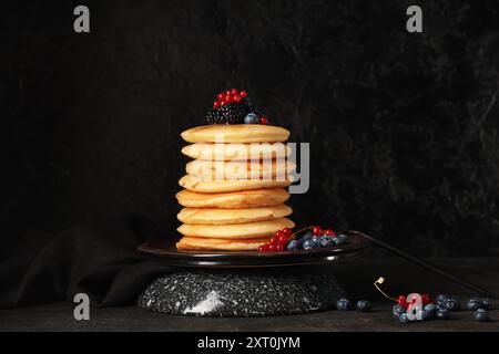 Piatto di frittelle dolci con diversi frutti di bosco freschi su sfondo nero Foto Stock