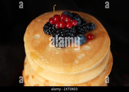 Frittelle dolci con diversi frutti di bosco freschi su sfondo nero, primo piano Foto Stock