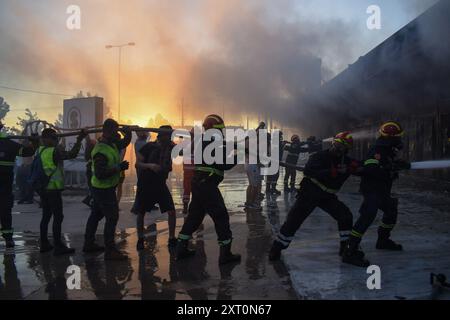 Atene, Grecia, 12 agosto 2024. I vigili del fuoco, aiutati da volontari, spengono l'incendio in un negozio nel sobborgo di Vrilissia, capitale greca. Un incendio che scoppiò a Varnavas l'11 agosto continuò a infuriare nell'Attica orientale il 12 agosto, si diffuse e si diffuse su un fronte che si estendeva per più di 20 chilometri. Diversi paesi hanno risposto positivamente alla richiesta delle autorità greche di assistenza da parte del meccanismo di protezione civile dell'UE (EUCPM) per combattere l'infuria degli incendi. Crediti: Dimitris Aspiotis/Alamy Live News Foto Stock