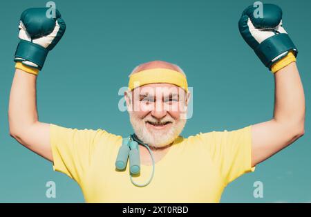 Il miglior allenamento cardiovascolare. Felice uomo anziano pugilato - primo piano ritratto. Attività ricreative. L'uomo anziano con i guanti batte il sacchetto di punzonatura. Un uomo figo anziano che combatte. IO Foto Stock