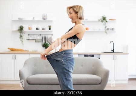 Donna felice in jeans oversize che mostra un successo nella perdita di peso Foto Stock