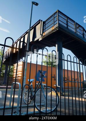 Anche il mondano può essere trasformato dalla bellezza nel momento e nel luogo giusti. Qui vedremo il ponte incombente sui binari di una stazione ferroviaria deserta di Radley Village, con una bicicletta nella pista ciclabile in primo piano Foto Stock