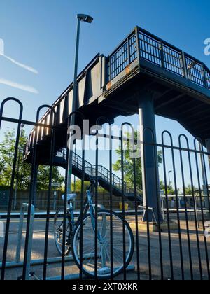 Anche il mondano può essere trasformato dalla bellezza nel momento e nel luogo giusti. Qui vedremo il ponte incombente sui binari di una stazione ferroviaria deserta di Radley Village, con una bicicletta nella pista ciclabile in primo piano Foto Stock