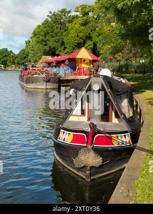 Abingdon sostiene di essere la città più antica d'Inghilterra. E il Tamigi attraversa il suo cuore. Qui vedremo una colorata casa galleggiante ormeggiata sulla riva nord del fiume, adiacente a Abbey Fields. Alle spalle ci sono due chiatte insolite che trasportano paraphernalia e tende per una fiera funebre che si sta allestendo sull'altra sponda del fiume. Foto Stock