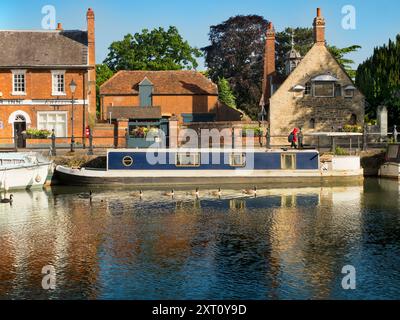 Saint Helen's Wharf è un famoso luogo di bellezza sul Tamigi, appena a monte del ponte medievale di Abingdon-on-Thames. Il molo è stato per secoli un importante collegamento di trasporto e trasporto marittimo sul Tamigi e tra i canali da Oxford e le Midlands. Belle case mercantili si incrociano con case di elemosina e la chiesa di Sant'Elena di epoca sassone. Qui vedremo imbarcazioni da diporto e case ormeggiate lungo le Long Alley Alms Houses, viste in una bella giornata di mezza estate dalla riva nord del fiume. E una fila di oche canadesi sceglie questo momento per nuotare... Foto Stock