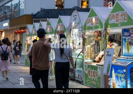 Suzhou, Cina - 11 giugno 2024: Una coppia cammina davanti alle bancarelle di cibo durante un festival serale a Suzhou, Cina. Foto Stock