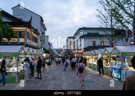 Suzhou, Cina - 11 giugno 2024: Un vivace mercato notturno a Suzhou, in Cina, con architettura tradizionale, bancarelle alimentari e venditori ambulanti che vendono prodotti di vario genere Foto Stock