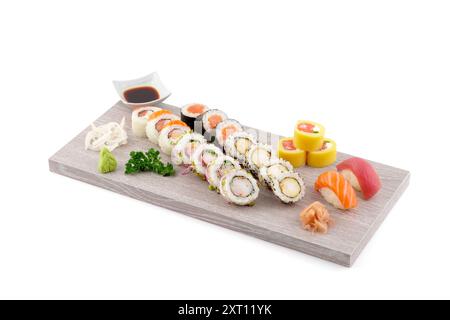 Una variegata selezione di sushi roll e pezzi di sashimi, disposti ad arte su un vassoio di legno da portata, abbinati a salsa di soia, wasabi e zenzero sottaceto Foto Stock