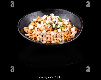 Deliziosi spaghetti saltati in stile asiatico con cubetti di tofu e funghi saltati con cipolle verdi tritate, serviti nuovamente in un'elegante ciotola nera Foto Stock