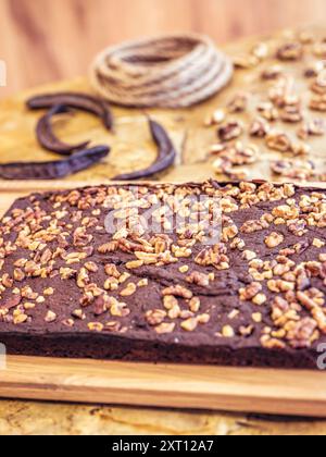 Ricca torta al cioccolato, generosamente condita con noci croccanti, esposta su un rustico tagliere in legno, accentuata da ferro di cavallo e corda nel Foto Stock