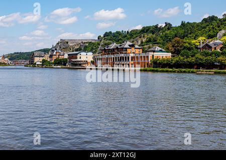 Il fiume Mosa con il paesaggio urbano di una località turistica sullo sfondo, la cittadella sulla cima della montagna rocciosa e le torri della chiesa collegiale di nostra Signora di Dinant, soleggiata Foto Stock