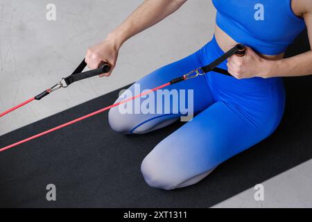 Una donna anonima si inginocchia su un tappetino per il fitness, allenandosi con una banda di resistenza, dimostrando il suo impegno per la forza della parte superiore del corpo Foto Stock