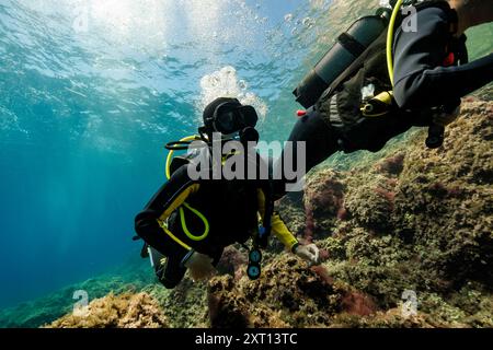 Subacquei attivi irriconoscibili in muta nera e maschere scuba diving in profondo oceano vicino alla barriera corallina mentre ti godi una vacanza a Minorca Foto Stock