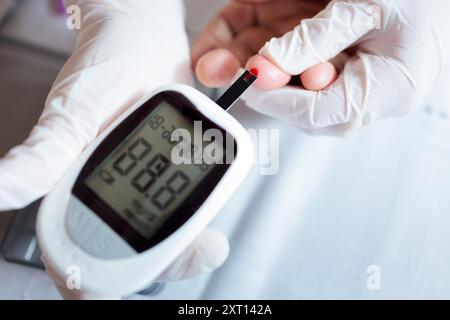 Un operatore sanitario misura i livelli di glucosio nel campione di sangue di un paziente utilizzando un glucometro digitale la lettura indica un livello basso di zucchero nel sangue, evidenziando Foto Stock