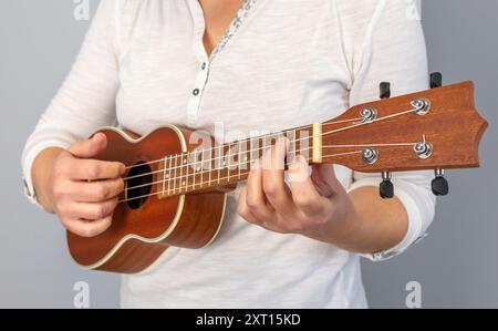 Primo piano anonimo di mani che suonano abilmente accordi su un ukulele, mostrando l'arte della musica e degli strumenti a corda Foto Stock