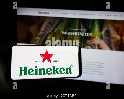 Persona che possiede uno smartphone con il logo della società olandese Heineken N.V. davanti al sito web. Mettere a fuoco il display del telefono. Foto Stock