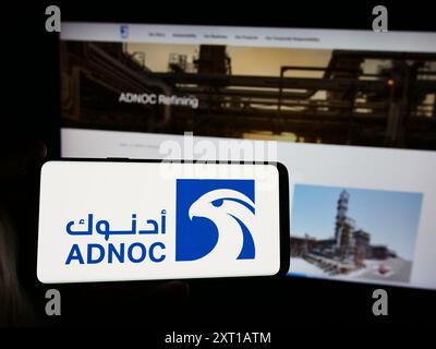 Persona con smartphone con logo dell'azienda petrolifera Abu Dhabi National Oil Company (ADNOC) davanti al sito Web. Mettere a fuoco il display del telefono. Foto Stock