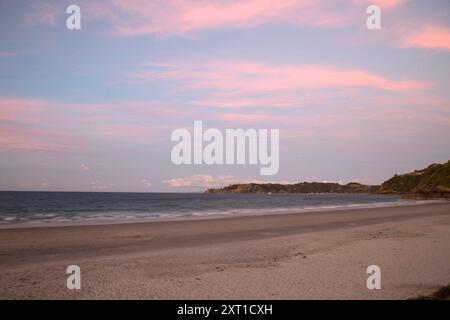 Le sfumature del sole proiettano un caldo bagliore su una spiaggia tranquilla con sabbia bianca soffice e onde calme sotto un cielo color pastello. Copyright evpe00613: XConnectxIma Foto Stock