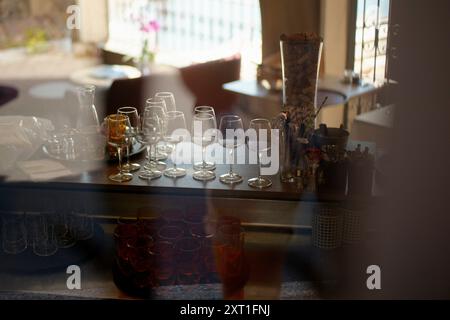 La luce solare serale filtra attraverso una finestra, diffondendo un caldo bagliore su un assortimento di bicchieri da vino vuoti disposti ordinatamente su un bancone del bar. Bola02479 Co Foto Stock