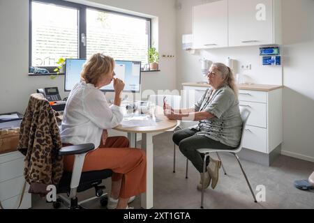 Diverse situatie in een huisartsenpraktijk Un professionista sanitario sta avendo una consultazione con una paziente anziana in un luminoso e moderno Foto Stock