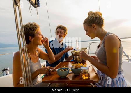 Gli amici si godranno un pasto su una barca a vela al tramonto con un paesaggio acquatico panoramico sullo sfondo. Stef00117 Copyright: XConnectxImagesx Foto Stock