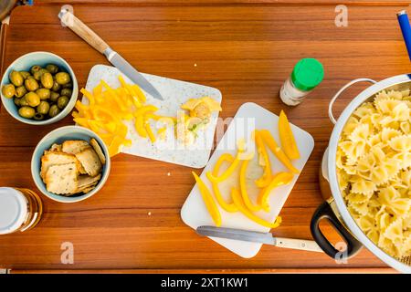 Un colorato scenario di preparazione della cucina con peperoni gialli tritati, olive, cracker e pasta cruda su una superficie di legno. Copyright stef00125: Foto Stock