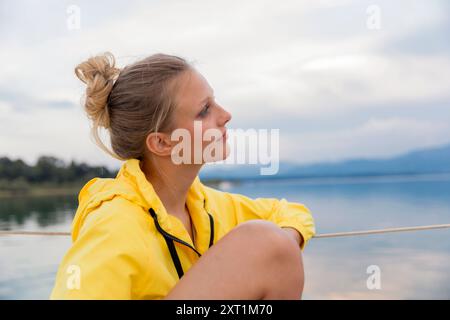 Donna con impermeabile giallo seduta accanto al tranquillo lago che guarda con attenzione all'orizzonte al tramonto. Stef00153 Copyright: XConnectxImagesx Foto Stock