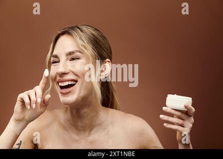 Una giovane donna con vitiligine sorride brillantemente mentre applica la crema al viso. Foto Stock