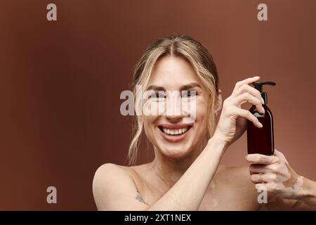 Una giovane donna con vitiligine sorride brillantemente mentre tiene in mano un flacone di prodotto per la cura della pelle su sfondo beige. Foto Stock