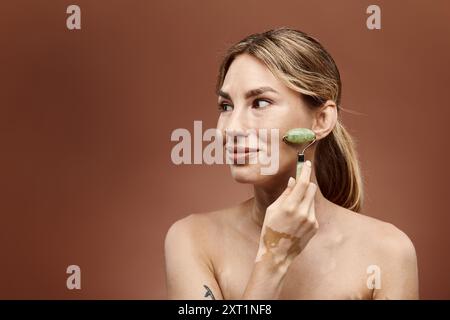 Una giovane donna con vitiligine usa un rullo di giada sul viso come parte della sua routine di cura della pelle. Lo sfondo è un beige morbido. Foto Stock