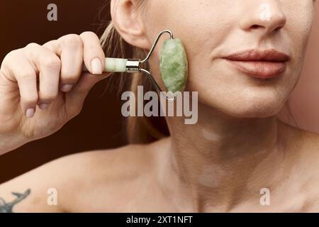 Una giovane donna con vitiligine usa un rullo di giada sul viso come parte della sua routine di bellezza e cura della pelle. Foto Stock