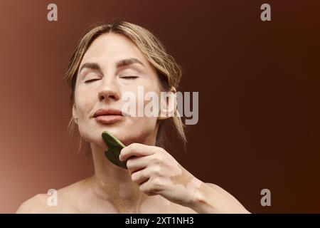 Una giovane donna con vitiligine utilizza una giada per una rilassante routine di bellezza. Foto Stock