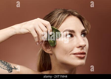 Una giovane donna con vitiligine usa una pietra di giada sul viso per una routine di cura della pelle. Foto Stock