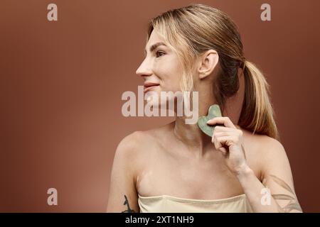 Una giovane donna con vitiligine utilizza uno strumento di bellezza in giada sul collo per una routine di cura della pelle. Foto Stock