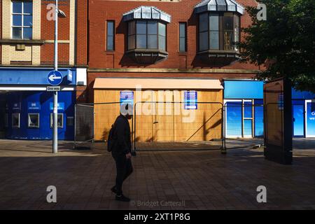 Hull, East Yorkshire, Regno Unito 13 agosto 2024. Ci sono stati 61 arresti con 22 accusati, e tre condannati con l'accusa di disordini violenti in mezzo a rivolte a Hull 10 giorni fa. Altri rimangono in custodia, in attesa di condanna. I negozi lungo Jameson St (direttamente di fronte alla stazione ferroviaria) e il Royal Hotel, che si credeva ospitasse i rifugiati, avevano le finestre rotte e furono saccheggiate. I negozi rimangono a bordo. Shoezone che ha subito più danni, è chiusa a tempo indeterminato. Oggi, la vita continua, con una maggiore presenza della polizia. NELLA FOTO: La zona scarpe rimane abbordata e chiusa. Bridget Catterall AlamyLiveNew Foto Stock