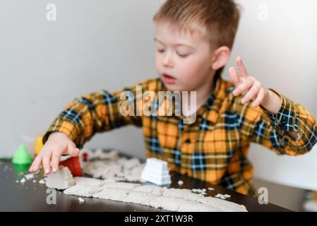 Un bravo ragazzo crea una torre di sabbia cinetica a casa. Il bambino gioca nella sandbox in camera Foto Stock