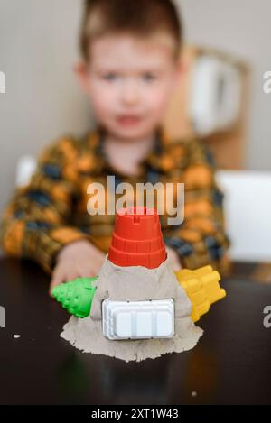 Un bravo ragazzo crea una torre di sabbia cinetica a casa. Il bambino gioca nella sandbox in camera Foto Stock