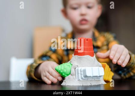 Un bravo ragazzo crea una torre di sabbia cinetica a casa. Il bambino gioca nella sandbox in camera Foto Stock