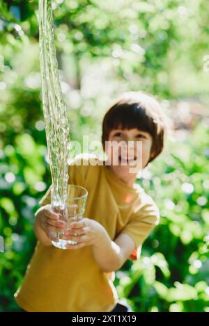 Un bel ragazzo versa l'acqua da un bicchiere in natura in una giornata di sole. Foto Stock