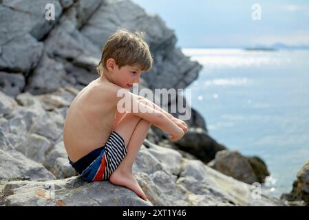 Un ragazzino siede sulla costa rocciosa con il mare sullo sfondo, guardando attentamente in lontananza. Hydra Greece bola02691 Copyright: XConnectxImag Foto Stock