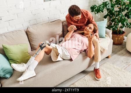 Una donna con una gamba protesica giace su un divano mentre il suo ragazzo si siede accanto a lei. Foto Stock